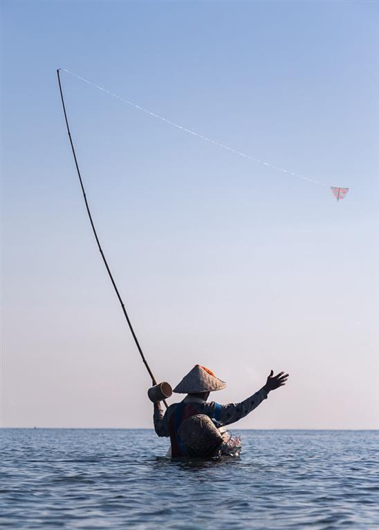 Southeast Asian man Fishing in waste deep water wearing a traditional hat.