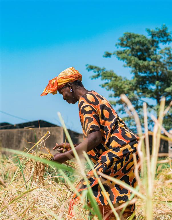 A fulani woman wearing a bright orange dress with cheetah print, standing in a field.